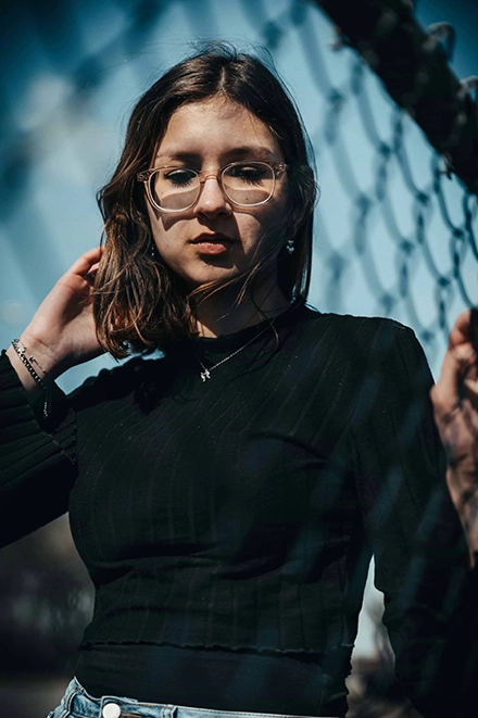 Portrait, en contre-plongée, d'une jeune femme brune à lunette à l'air contemplatif.