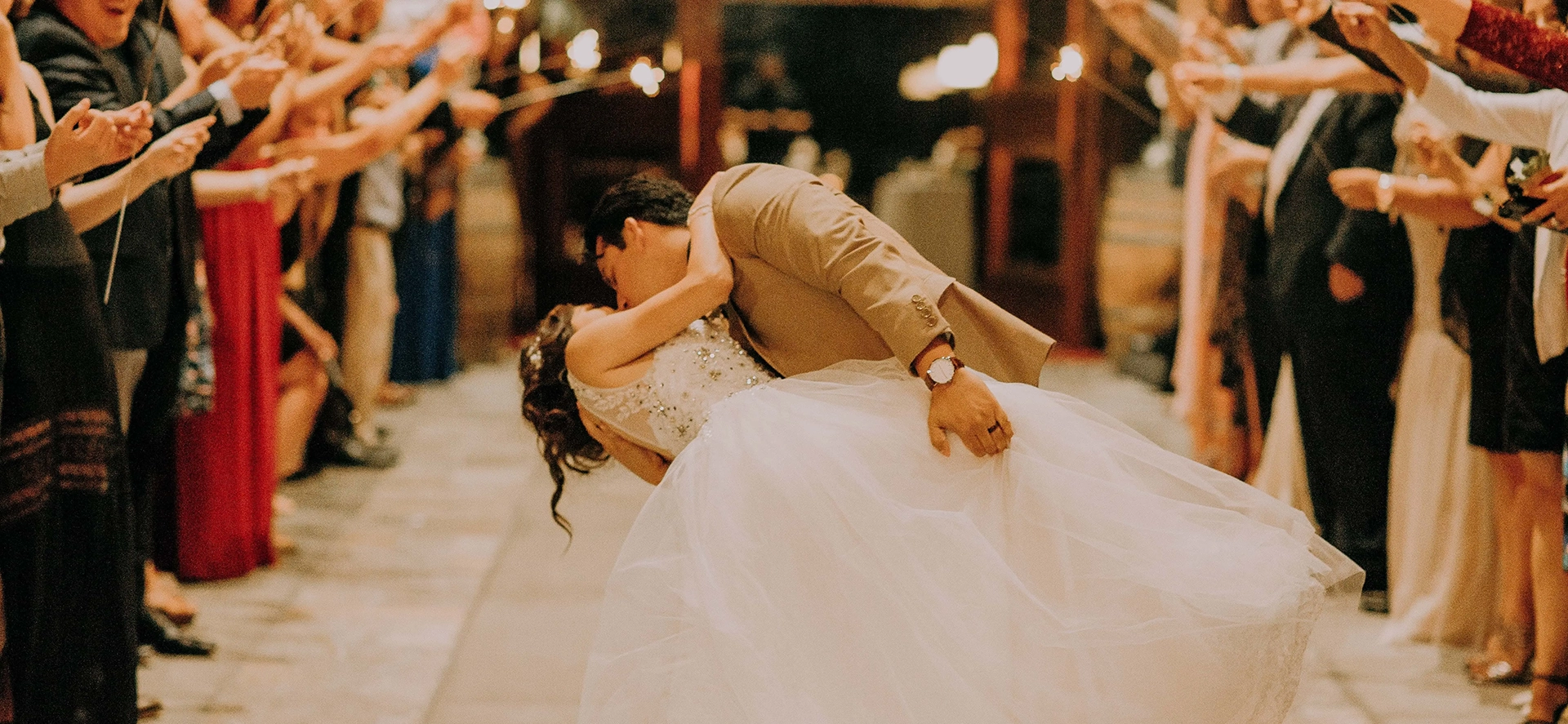 Photographie d'un couple de jeunes mariés, en train de s'embrasser, au milieu de l'allée nuptiale.