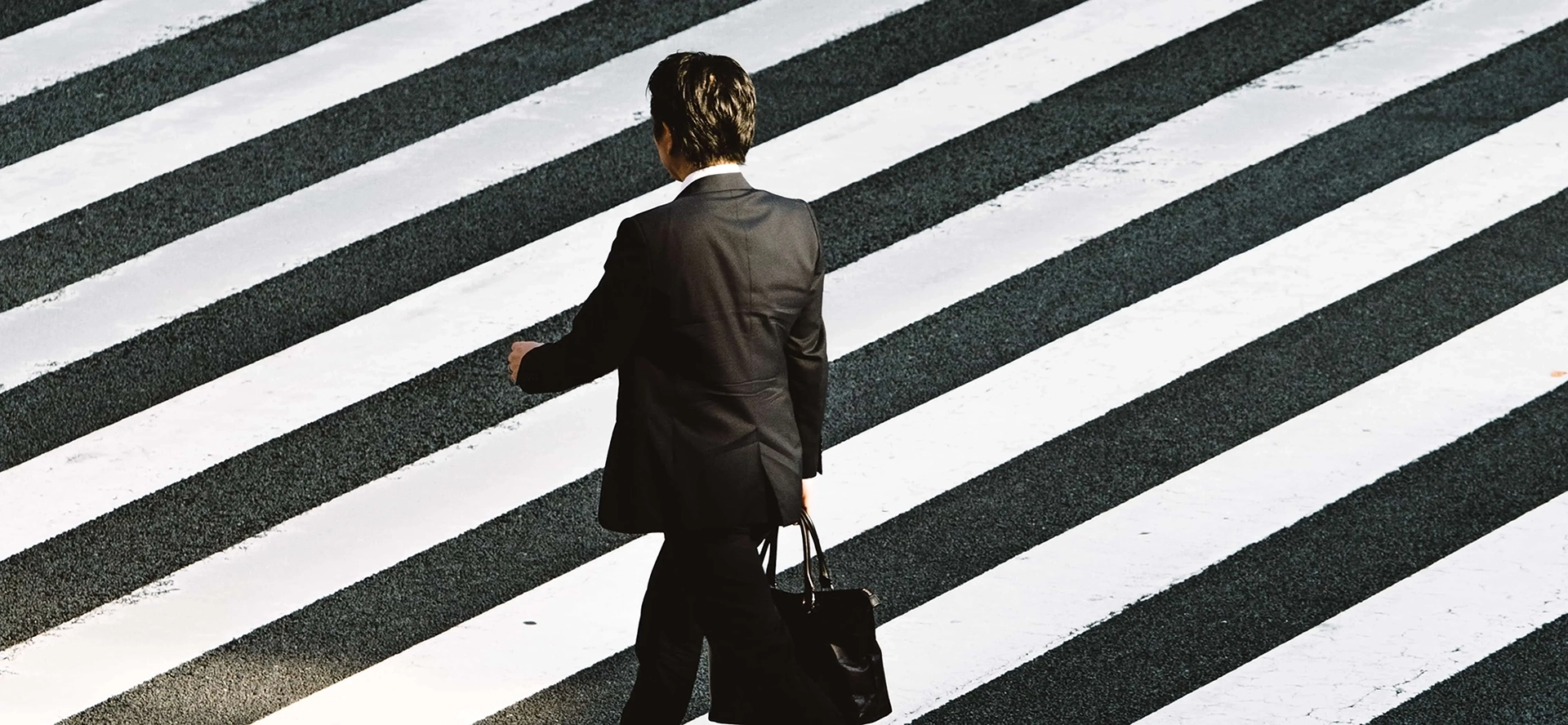 Photographie d'un homme traversant la rue, de dos, tenant sa malette.